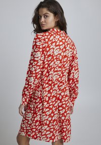Rochie roșie cu un model abstract alb, mâneci lungi și talie strânsă. Prezintă o croială lejeră și un material moale, ușor.