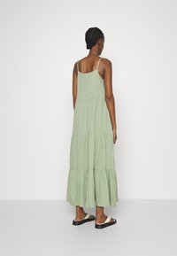 Robe maxi verte à volants avec bretelles spaghetti réglables et un ourlet fluide. Le tissu a une apparence texturée et une coupe décontractée.
