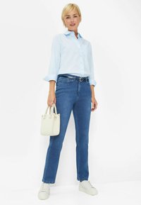 Camicia a maniche lunghe blu chiaro, jeans blu scuro, sneakers bianche e una piccola borsa leggera. Presenta una cintura e una tasca sulla camicia.