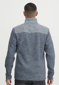 Mėlynas ir pilkas šiltas megztinis su aukštu apykakle ir ilgomis rankovėmis. Audinys turi melužtą raštą; nugarinė dalis yra paprasta ir nepuošta.