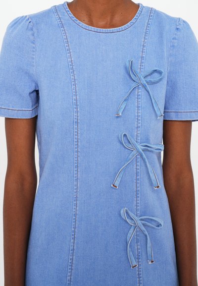 Light blue denim dress with short puff sleeves, featuring three bows down the front and contrasting stitching along the seams.