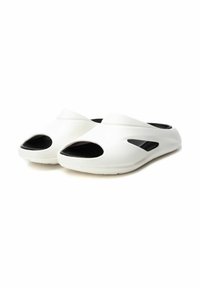 Zapatos blancos sin cordones con punta abierta y diseño recortado. Hechos de material suave con un interior negro y suela texturizada para mayor agarre.