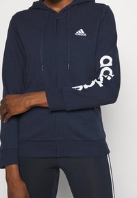 Mörkblå zip-up hoodie i mjukt tyg. Har en dragkedja i huven, framfickor och vitt logotryck på vänster ärm.