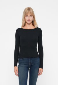 Svart langermet topp med båtutringning, slim fit, myk stoff og glatt tekstur, paret med mørkeblå jeans.