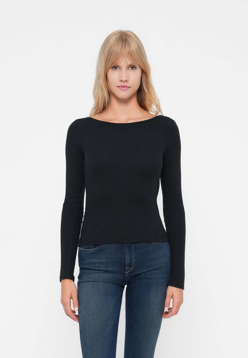 Svart langermet topp med båtutringning, slim fit, myk stoff og glatt tekstur, paret med mørkeblå jeans.