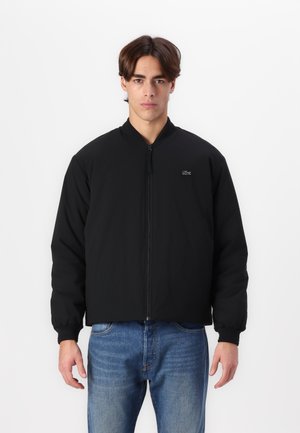 Black bomber jacket with a stand-up collar, zip closure, and elastic cuffs. Features a small logo on the chest and a loose fit.