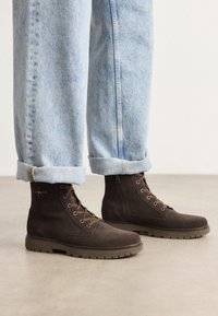 Stivaletti in suede marrone con finitura testurizzata, suole in gomma e chiusura a cerniera, indossati con jeans azzurri chiari risvoltati.