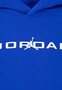 Sweatshirt com capuz azul, apresentando um grande texto branco "JORDAN" e um emblema de uma figura a saltar, feito de tecido suave.
