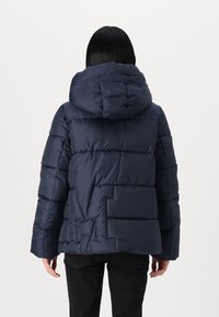 Mornarska puhovka s kapuco, z dvignjenim dizajnom in vidnim šivi. Gladka tekstura, sproščen kroj in stranske žepe.