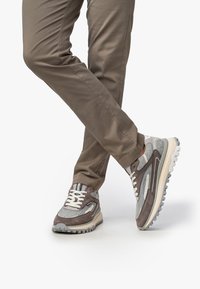 Scarpe sportive grigie con un mix di suede e rete, dotate di una suola spessa, lacci bianchi e accenti decorativi in un beige chiaro.