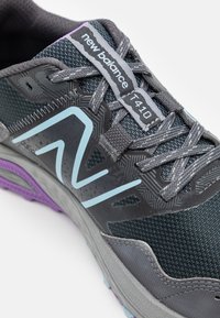 La sneaker New Balance 410 para hombres presenta una parte superior de malla gris, un logo azul claro, paneles con un diseño estampado y una suela con acentos morados.