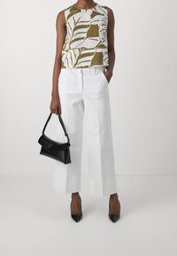 Top court sans manches avec un motif de feuilles vertes et blanches, associé à un large pantalon blanc. Un sac à main noir et des talons aiguilles noirs complètent le look.