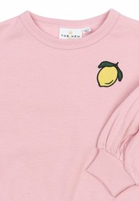 Gaiši rozā garām piedurknēm krekls ar ribotām aprocēm, apaļu kakla izgriezumu un mazu izšūtu dzeltenu citronu ar zaļām lapām uz krūšu daļas.