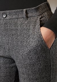 Grå byxor med hundtandsmönster i texturerat tyg, utrustade med en framficka och en enkel knappstängning i midjan.