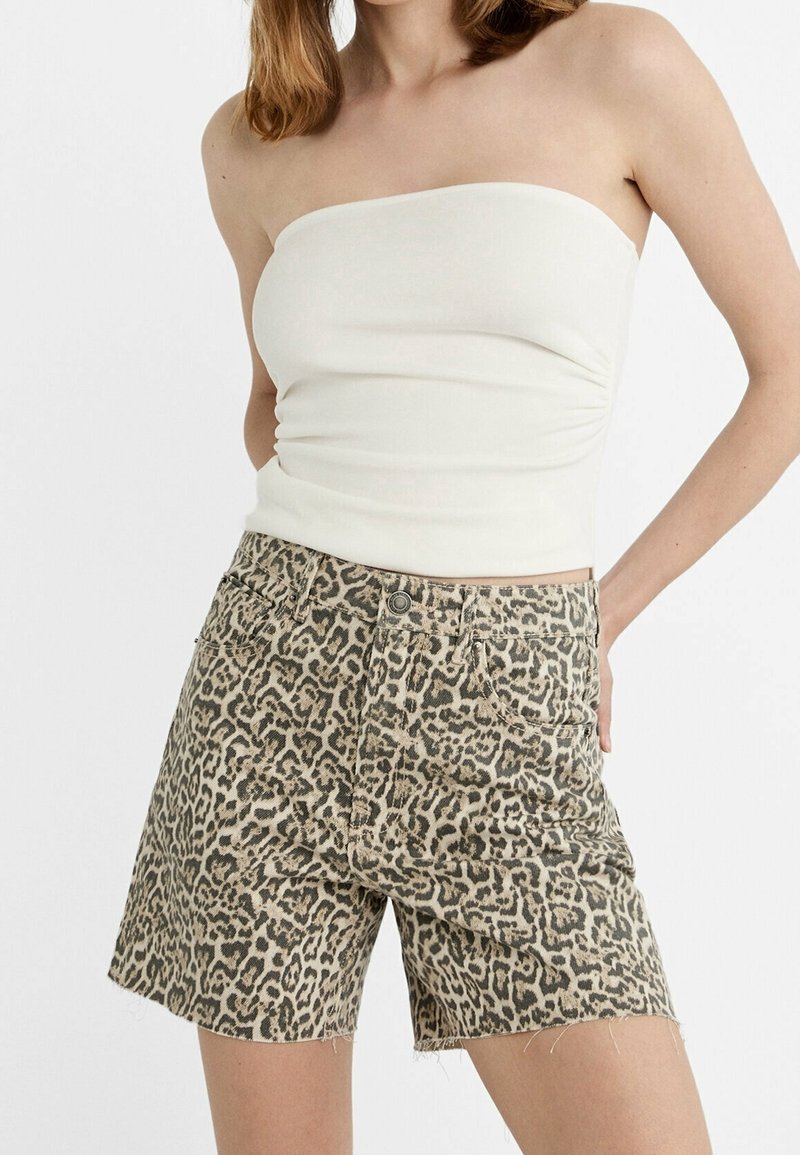 Shorts en jean imprimé léopard tan avec des bords effilochés, associés à un top blanc sans manches. Les shorts disposent de poches avant et d'une fermeture à bouton en métal.