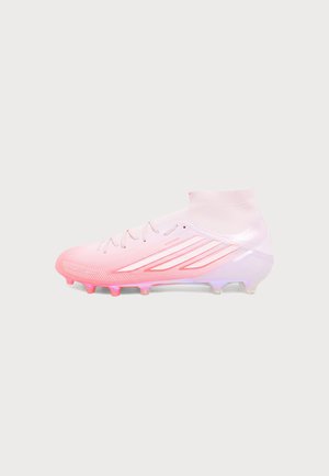 Crampon de football montante blanc et rose avec lacets et crampons sous la semelle, montré de côté sur un fond uni.