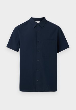Chemise bleu marine à manches courtes avec col pointu et poche poitrine gauche, présentée sur un fond gris clair.