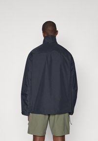 Veste imperméable navy avec un col haut, des épaules tombantes et une coupe décontractée. Texture mate sans matériel ou motifs visibles.