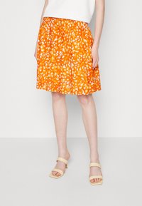 Orange kjol med blommönster, elastisk midja, knälång, tillverkad av lätt material, i kombination med beige sandaler med fyrkantig tå.