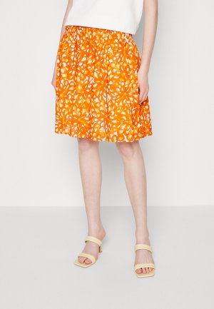 Jupe orange à motif floral, taille élastique, longueur genou, en tissu léger, assortie à des sandales beiges à bout carré.