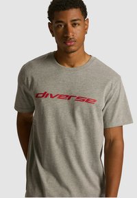 Szara bawełniana koszulka z krótkim rękawem, z wyrazistym czerwonym logo "diverse" na piersi. Miękka w dotyku, o luźnym kroju.