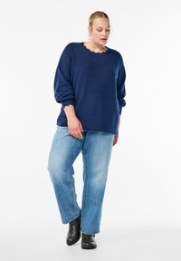 Navy blue knit sweater with a scalloped neckline, paired with light-wash jeans and black ankle boots. Soft texture and relaxed fit.