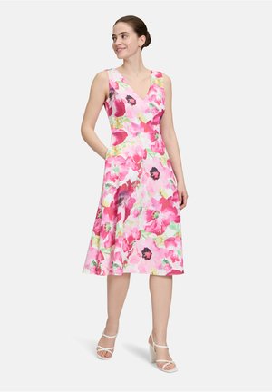 Bloemenjurk met een V-halslijn, voorzien van een roze en groene aquarelpatroon, een uitlopende rok en zijzakken. Draag het met witte blokhakken.