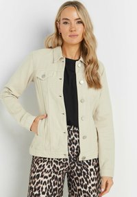 Beige denimjacka med knäppning fram, spetsig krage och två bröstfickor. Har långa ärmar och en avslappnad passform, kombinerad med mönstrade byxor.