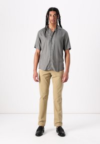 Short-sleeve, gray button-up shirt made of smooth fabric. Paired with beige pants and black loafers, standing against a white background.