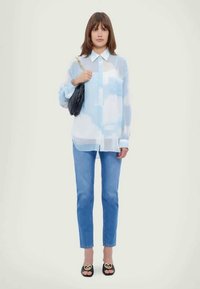 Camisa azul translúcida de botões com padrões de nuvens, colarinho branco, combinada com jeans azul claro e sandálias deslizantes pretas com detalhes de corações.