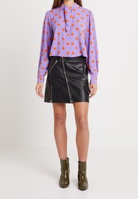 Blusa viola a maniche lunghe con pois arancioni, abbinata a una gonna in pelle nera con zip e stivaletti alla caviglia in vernice verde.