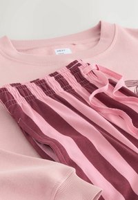 Jasnoróżowy sweatshirt z prążkowanymi mankietami i dekoltem, zestawiony z spodniami w paski w kolorze bordowym i różowym, które mają elastyczny pas i sznurek.
