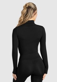 Top crop à manches longues noir en tissu lisse et extensible, avec un col montant et une coupe ajustée, associé à un legging taille haute assorti.