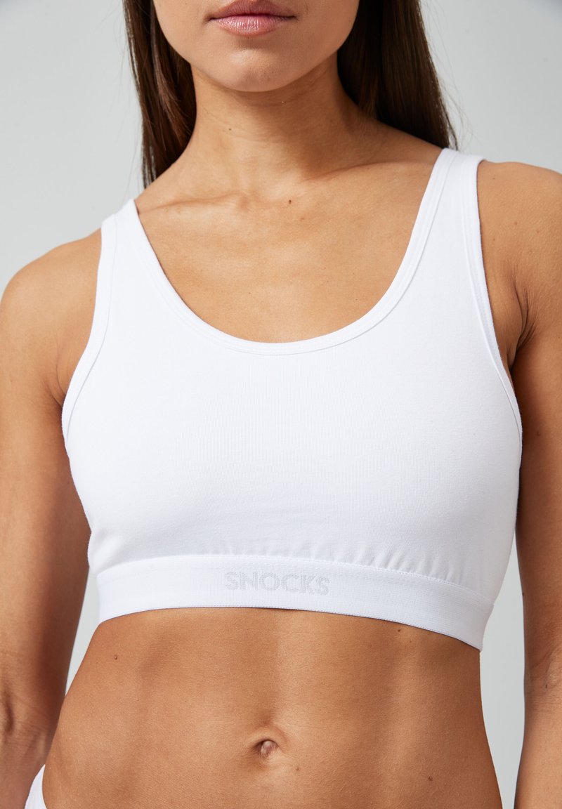 Witte katoenen sport-bh met een gladde textuur, brede banden en een logo-band aan de rand. Minimalistisch ontwerp, geschikt voor sportkleding.