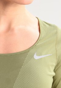 Nahaufnahme einer Person, die ein hellgrünes, strukturiertes Nike-Sportoberteil mit einem weißen Swoosh-Logo nahe dem Schlüsselbein trägt.