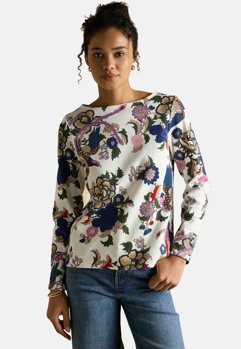 Długa bluzka z długim rękawem w kwiatowy wzór, w kolorze białym, z niebieskimi, różowymi i zielonym akcentami. Gładka tekstura, okrągły dekolt i luźny krój.