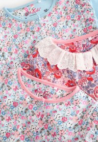 Three cotton children's tops with floral patterns in blue, pink, and red. Includes a ruffled collar and colorful trims. Labels visible.