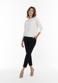 Fehér kötött kardigán kerek nyakkivágással, gombos előrésszel, fekete slim-fit nadrággal és bézs magassarkúval párosítva.