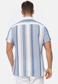 Camisa de manga corta en blanco con rayas verticales azules, con cuello y tejido texturizado. La parte de atrás tiene un diseño liso con un dobladillo recto.