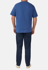 Niebieska koszulka z krótkim rękawem z okrągłym dekoltem, zestawiona z ciemnoniebieskimi dżinsami i jasnymi trampkami. Materiał koszulki wydaje się gładki i swobodny.