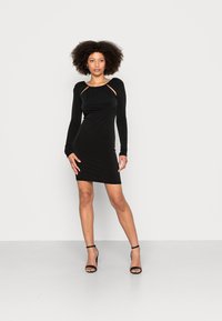 Vestido bodycon preto com mangas longas, decote franzido e recortes nos ombros. Textura suave, comprimento até ao joelho, silhueta ajustada.