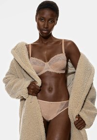 Ensemble de soutien-gorge et culotte en dentelle beige avec des bords festonnés, associé à un peignoir en peluche beige. Les matériaux texturés créent un look doux et superposé.