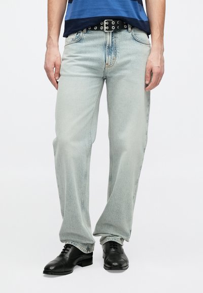 Ανοιχτό μπλε τζιν τζιν με χαλαρή εφαρμογή, με ξεθωριασμένη υφή, πέντε τσέπες και μαύρη ζώνη με αγκράφα, συνδυασμένα με μαύρα επίσημα παπούτσια.