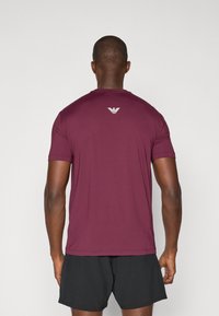 Μαρουλί αθλητικό μπλουζάκι κοντό μανίκι με στρογγυλή λαιμόκοψη και μικρό λευκό λογότυπο στο πάνω μέρος της πλάτης, συνδυασμένο με μαύρες βερμούδες.