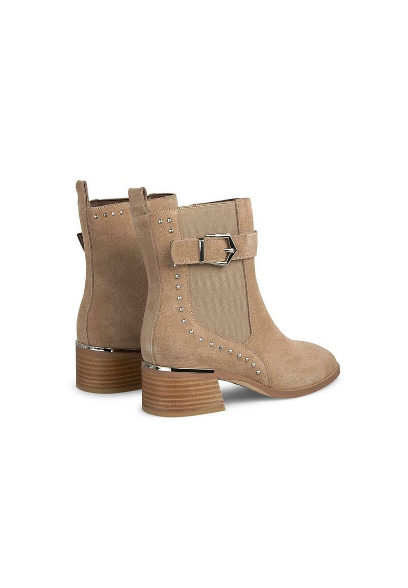 Beige Wildleder Stiefeletten mit seitlichen Einsätzen, silbernen Schnallenakzenten, Nietenverzierungen und einem Blockabsatz mit holzähnlicher Optik.