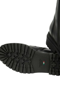 Stivali neri in pelle con suola resistente dotata di motivi di trazione incrociata. Include una cerniera sul lato e un'etichetta di marca sulla suola.