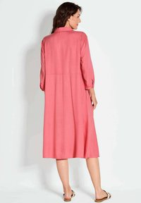 Langes, pinkfarbenes Kleid aus leichtem Stoff, mit einem Kragen, drei Viertelärmeln und einem lockeren, fließenden Design. Einfach und in Einfarbigkeit.