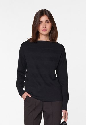 Zwarte gebreide trui met een bootnek, lange mouwen en subtiele horizontale textuurdetails. Gecombineerd met donkere broek.