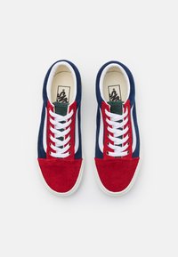 Zapatillas de pana rojo y azul marino con rayas blancas, cordones blancos, detalles verdes y diseño de corte bajo. Tejido texturizado y suela de goma.