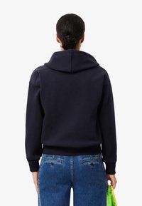 Navy blue hoodie with a large, structured hood and ribbed cuffs, paired with light blue high-waisted jeans featuring back pockets.
